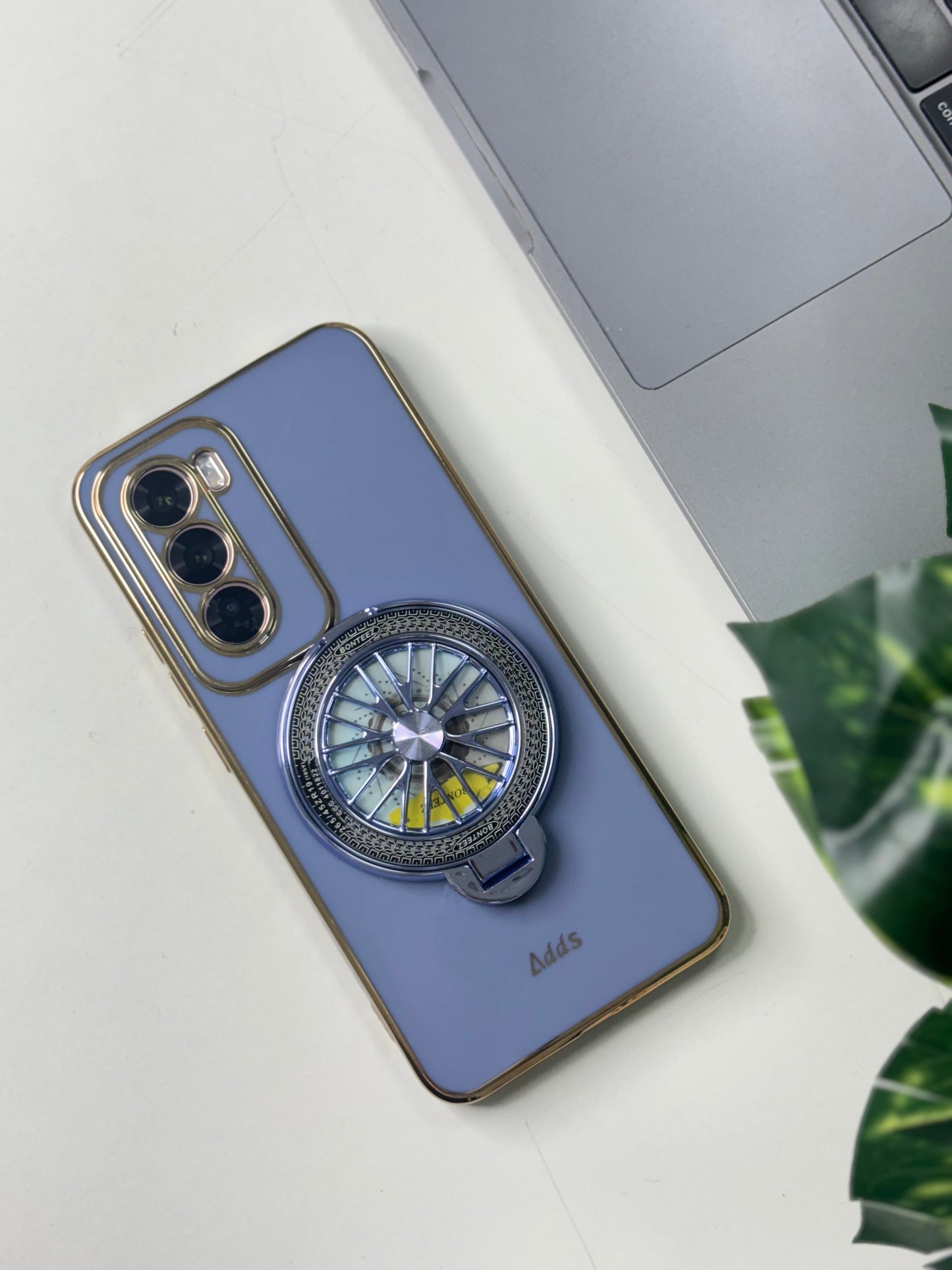 A blue silicone oppo reno 12 pro case with a decorative element on the back, placed on a table next to a laptop and a plant.